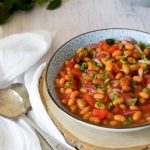 Baked Bean salad in a blue bowl on a piece of wood with spoons on left