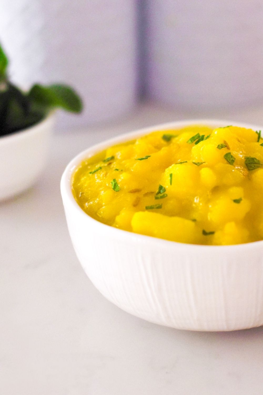 Potatoes cooked with turmeric in a white bowl with a few mint leaves on the side