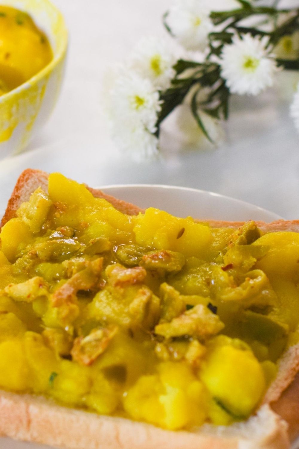 Potato Curry on a slice of white bread with flowers on the right and a bowl on the left