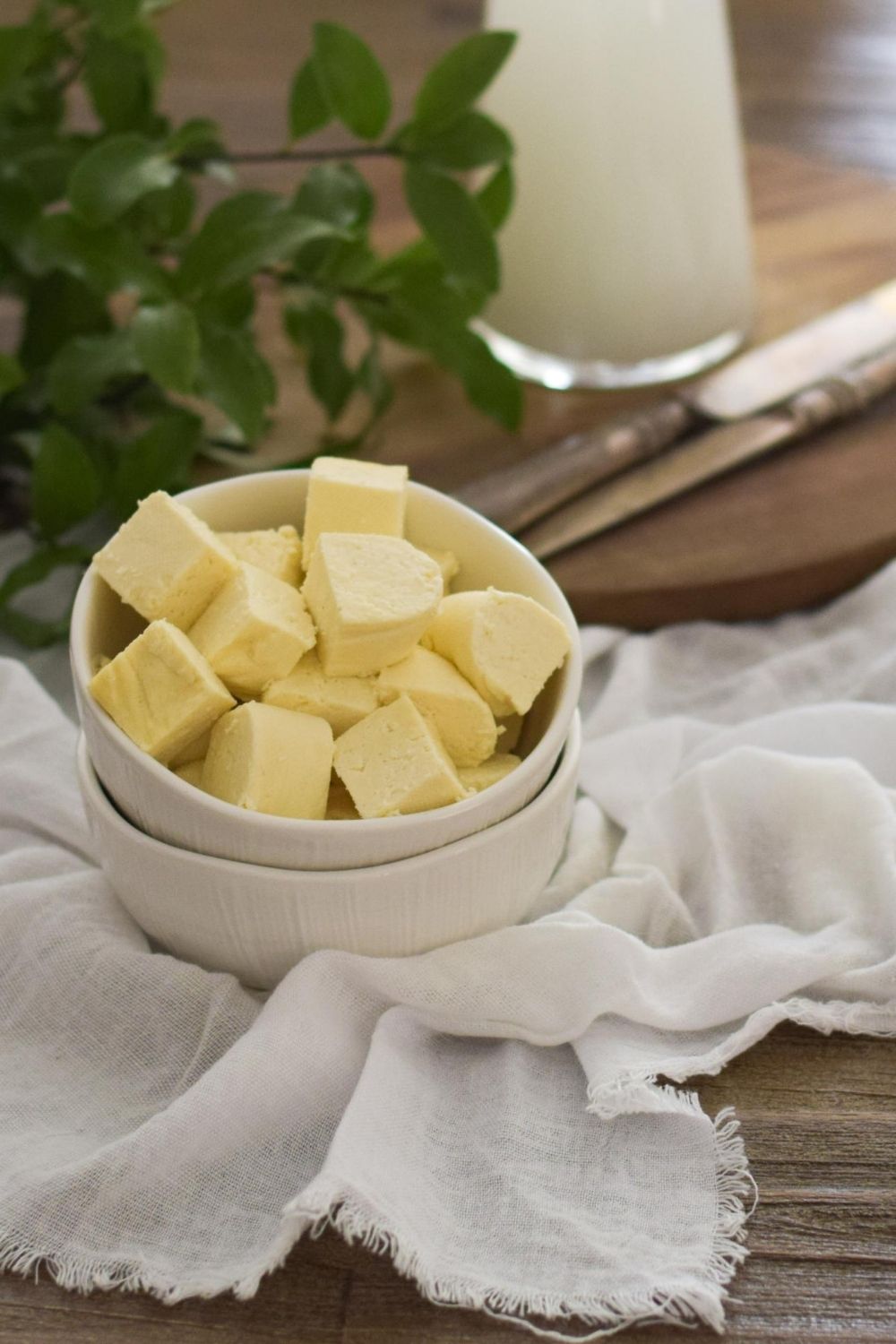Cubed paneer in a white bowl with knives and milk behind
