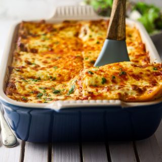 Lamb lasagna in a blue casserole dish with a blue spatula