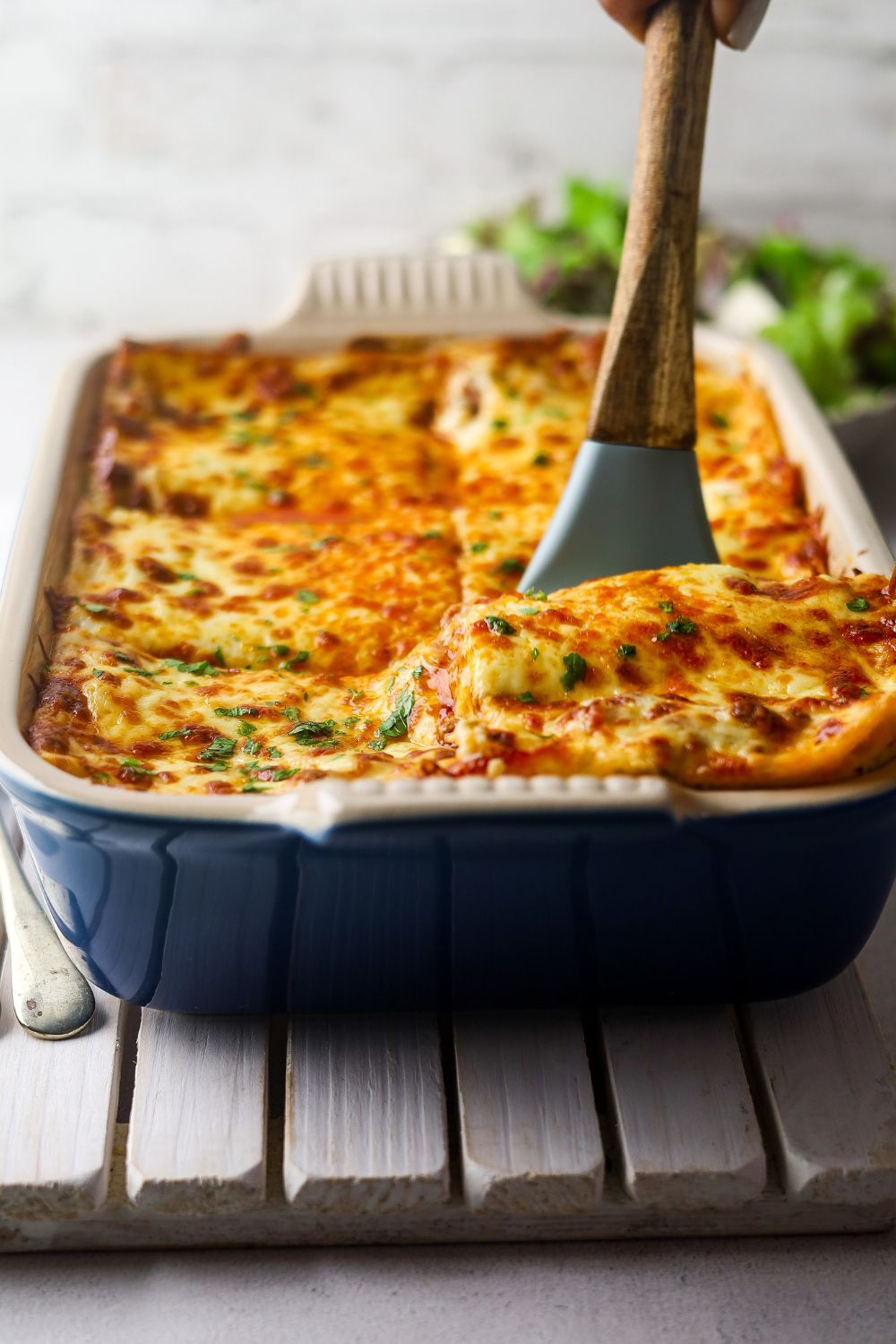 Lamb lasagna in a blue casserole dish with a blue spatula