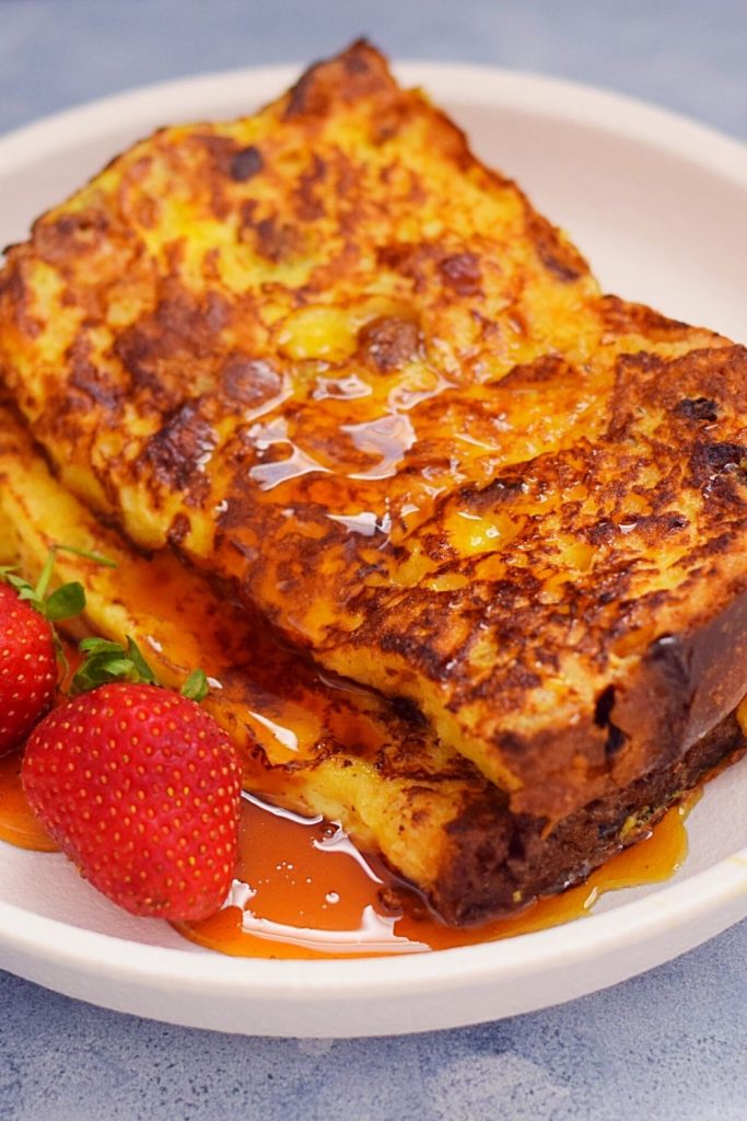 Panettone French Toast on a white plate with strawberries and maple syrup