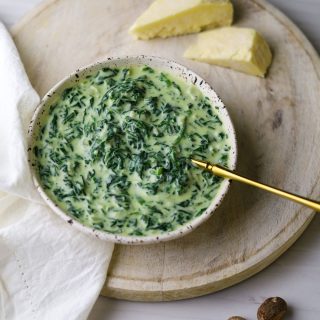 Creamed spinach in a white bowl on a white board with cheese on the top right