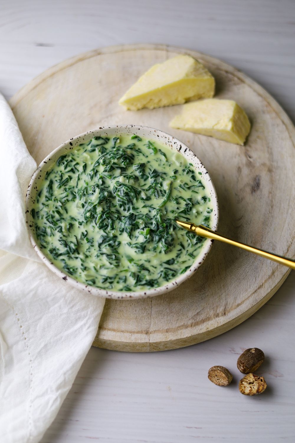 Creamed spinach in a white bowl on a white board with cheese on the top right 