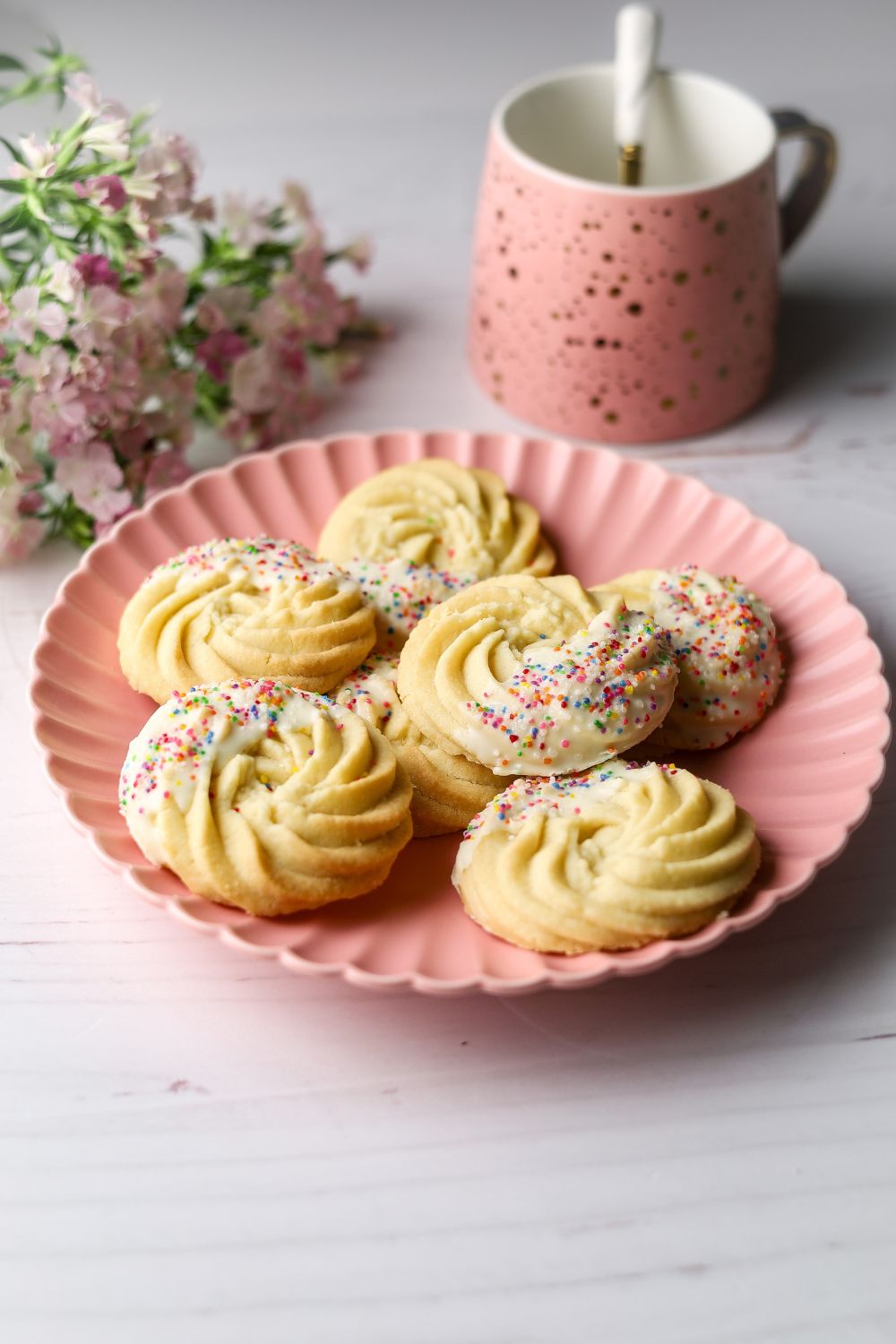 Butter Cookies on a pink plate with a pink cup on the top right and pink flowers on top left