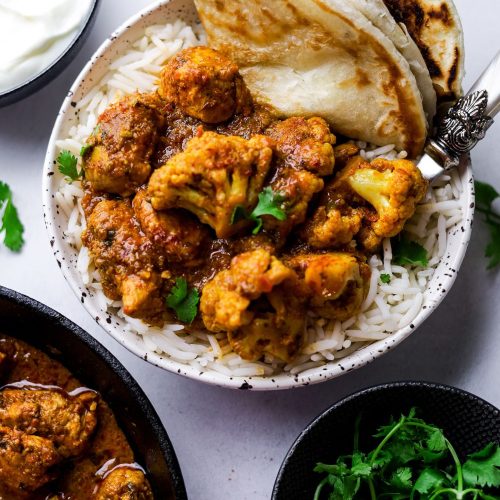 Cauliflower and Chicken Curry in a white bowl with rice and paratha