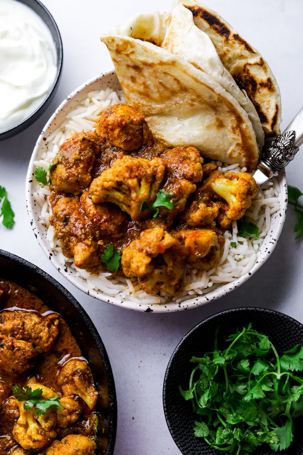 Cauliflower and Chicken Curry in a white bowl with rice and paratha