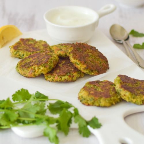 Broccoli Fritters on a white board with yogurt on the right and coriander on the bottom left
