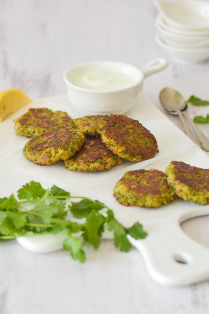 Broccoli Fritters on a white board with yogurt on the right and coriander on the bottom left