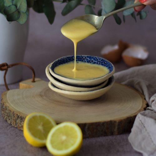 Hollandaise sauce in a blue bowl with egg shells right back and lemons in front
