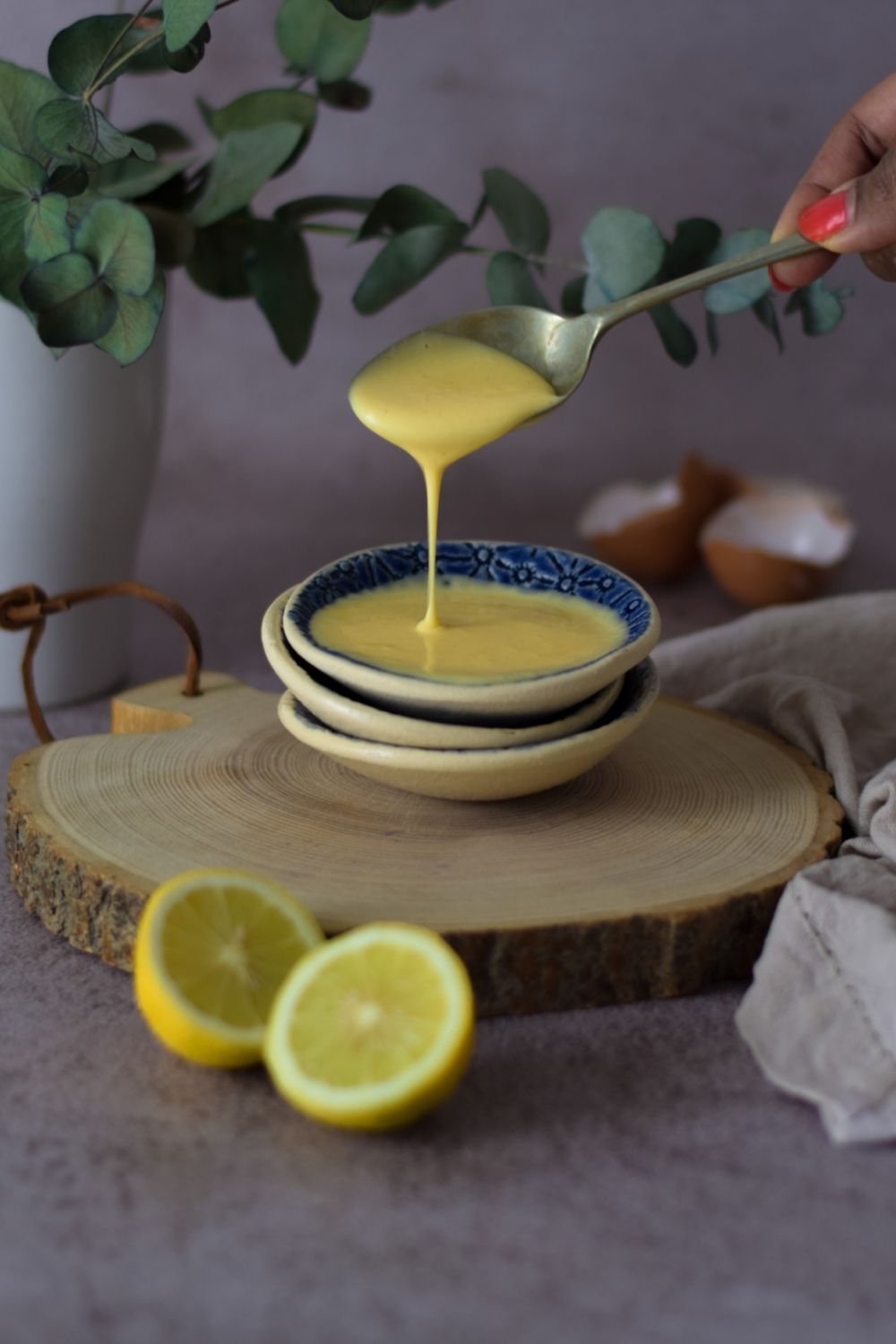 Hollandaise sauce in a blue bowl with egg shells right back and lemons in front