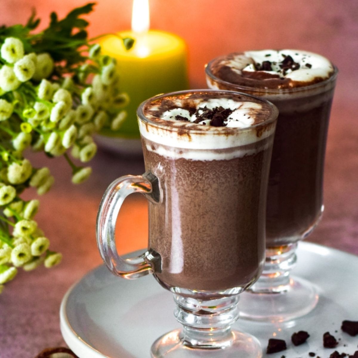 Two mugs of hot chocolate with flowers and candle on the left