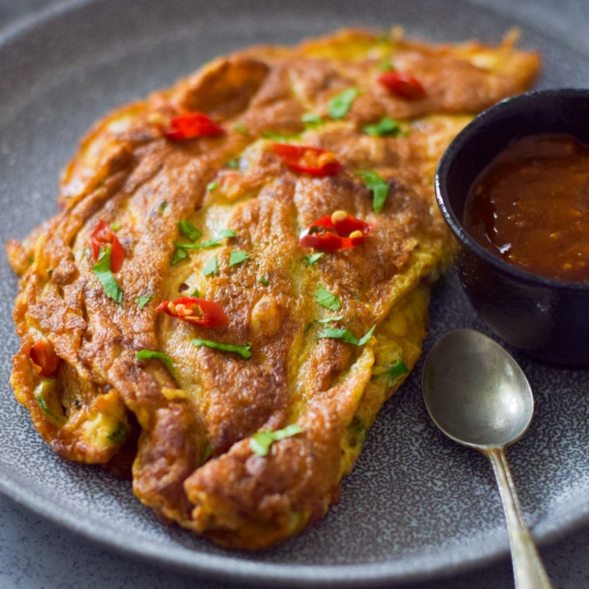 Spicy Masala Omelette on a plate with sauce and spoon on the right