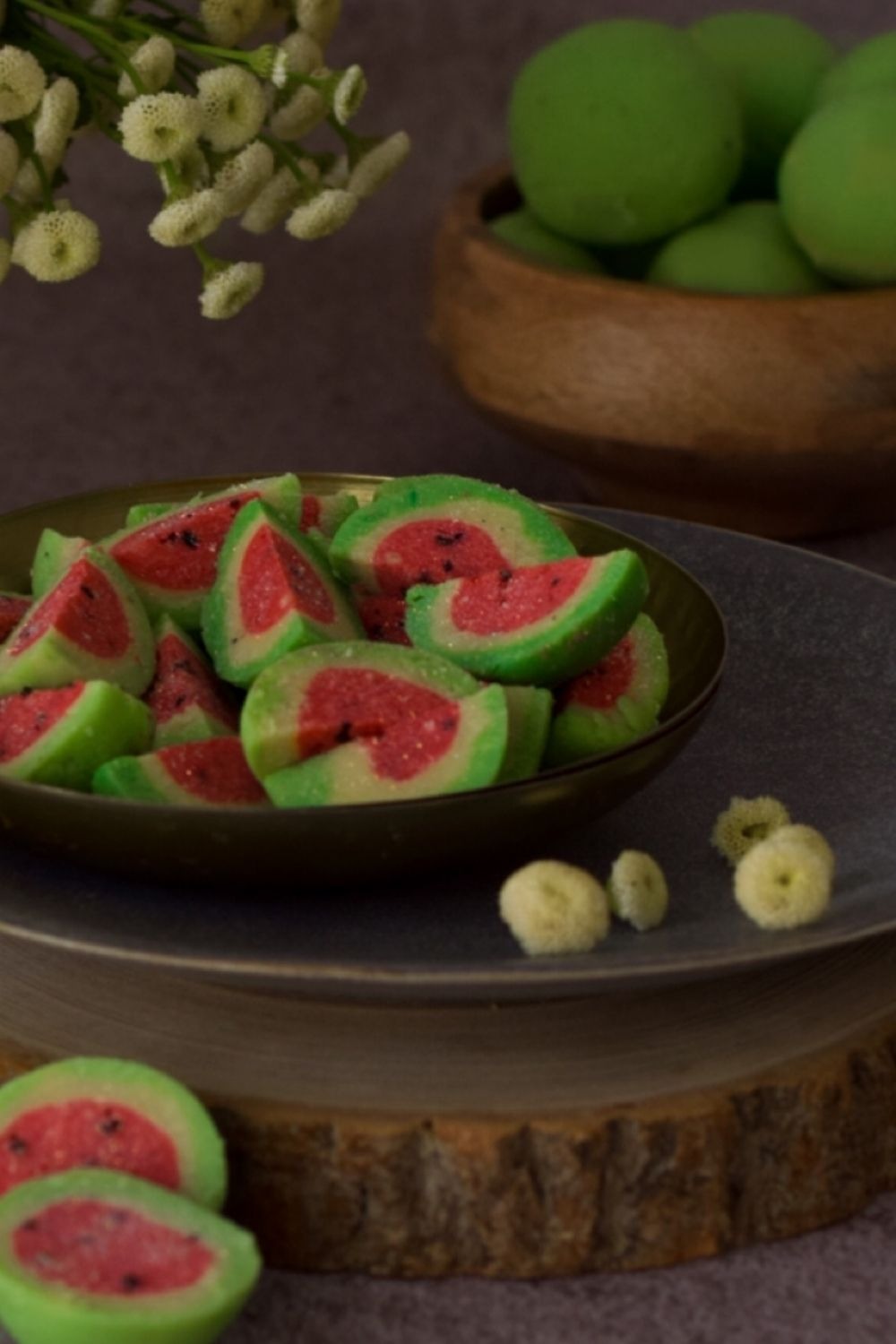 Watermelon shaped burfee in a black plate with flowers on left 