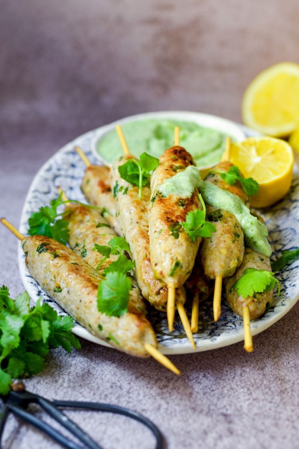 Chicken Seekh Kebabs in a blue and white platter with herb scissor bottom left and lemon top right