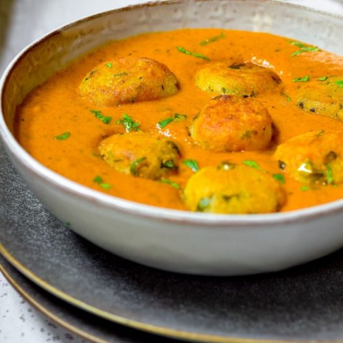 Malai Kofta in a white bowl on top of black plates with coriander at the back