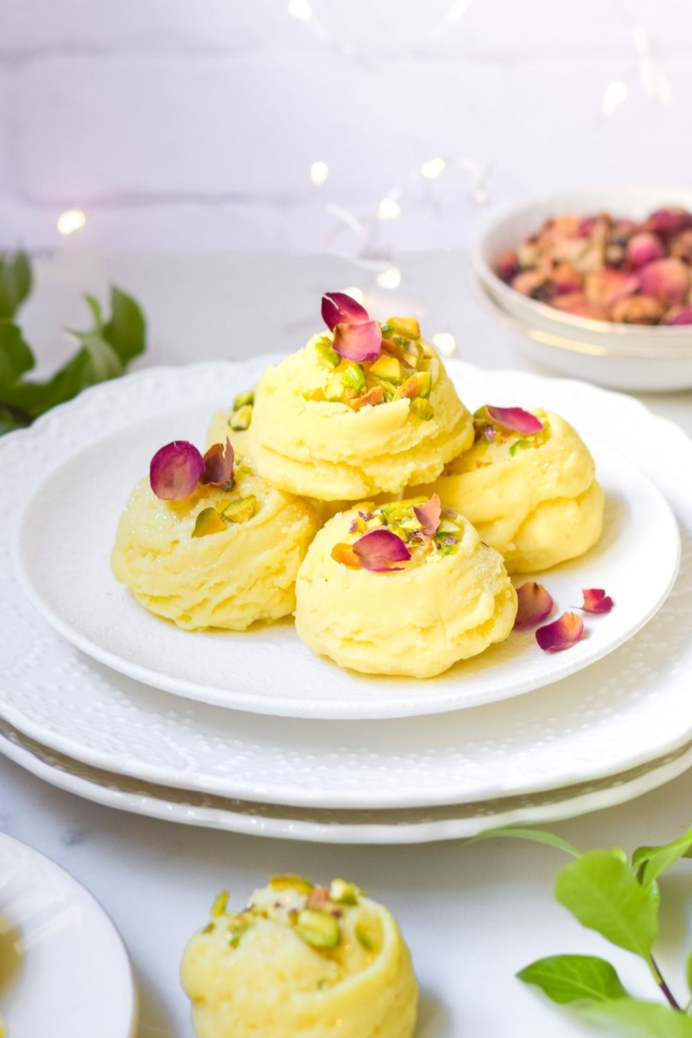 Rose Pistachio Burfee Mithai in a white plate with roses at the back right