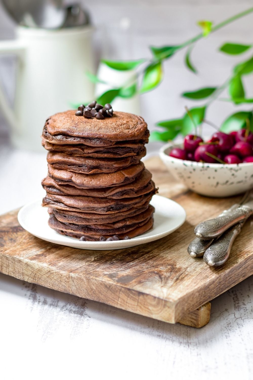 Fluffy chocolate pancakes on a white plate with cherries on the side