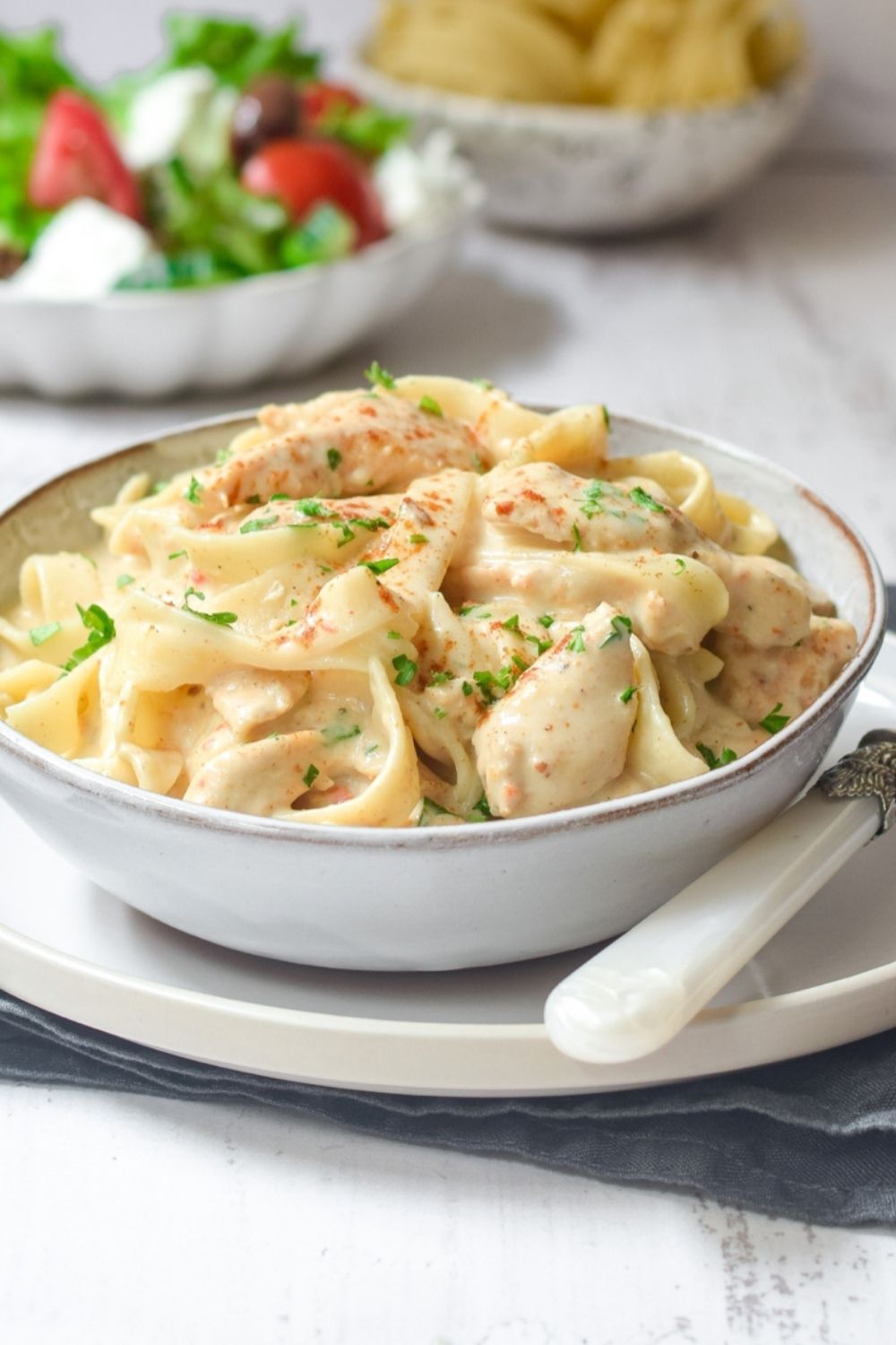 Creamy Chilli Garlic Chicken Pasta in a white bowl with salad on the left