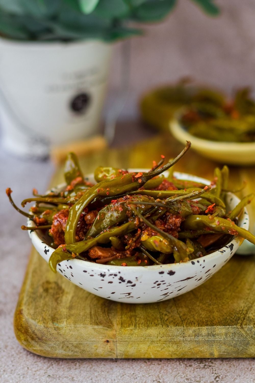 Pickled chillies in a white speckled bowl on a wooden board