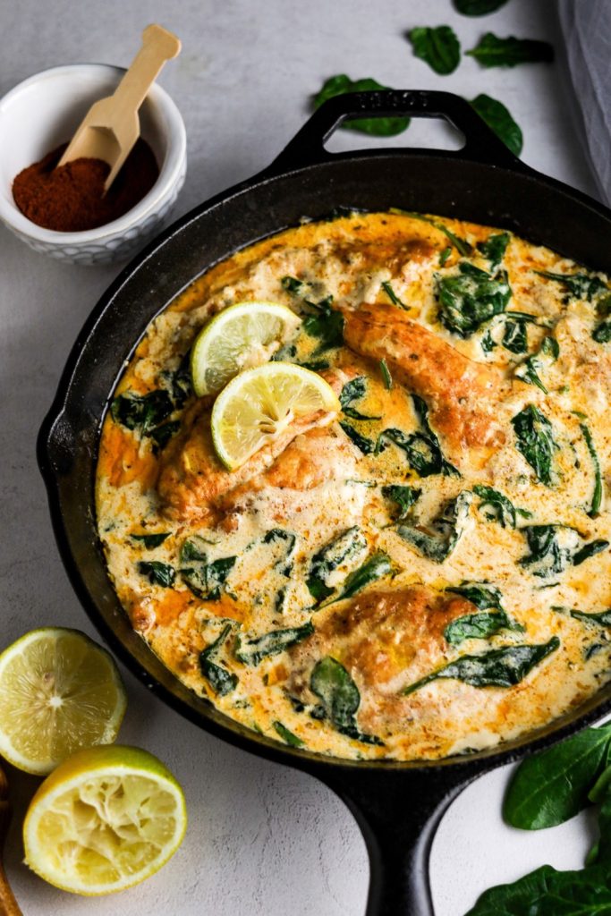 Creamy Lemon Chicken with Spinach in a black cast iron pan with lemon on the left bottom and paprika top left