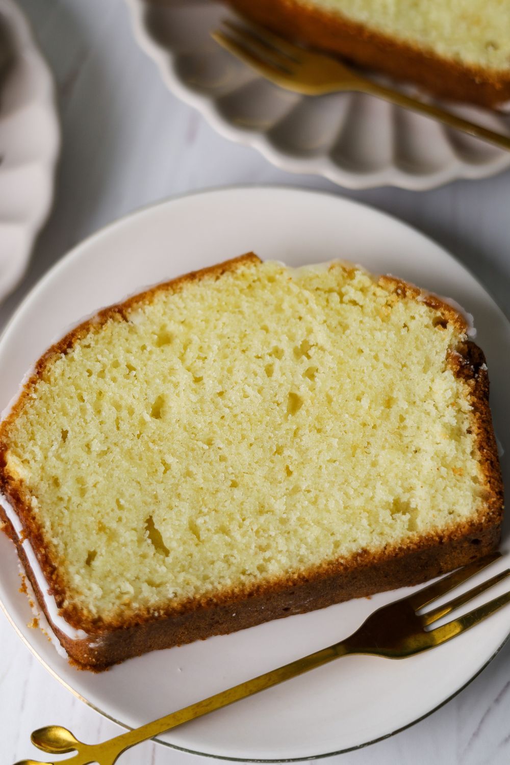 A slice of lemon loaf on a white plate with a fork on the right