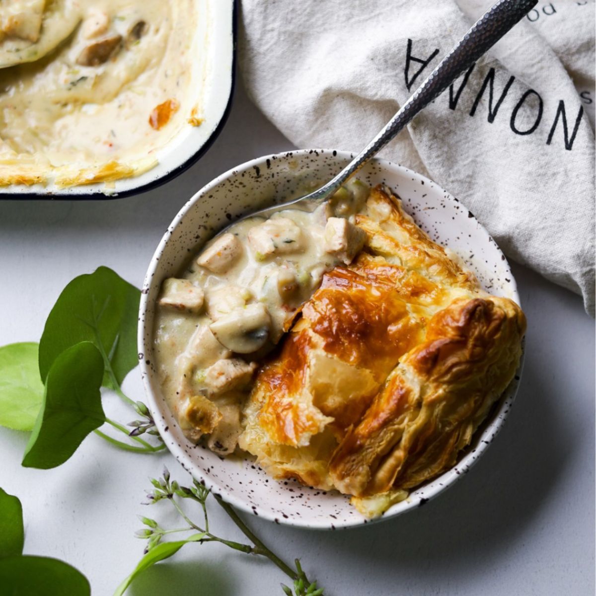 Chicken Leek Mushroom Pot Pie in a white bowl with leaves bottom left and a kitchen towel on top right