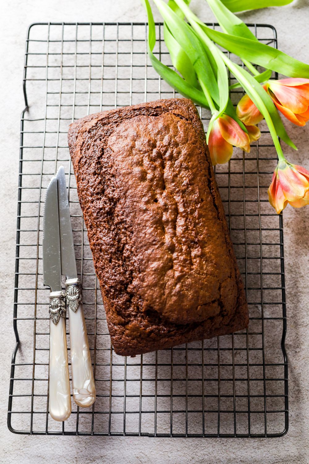 Chocolate Fudge Loaf in a wire cooling rack with 2 knifes on the left side